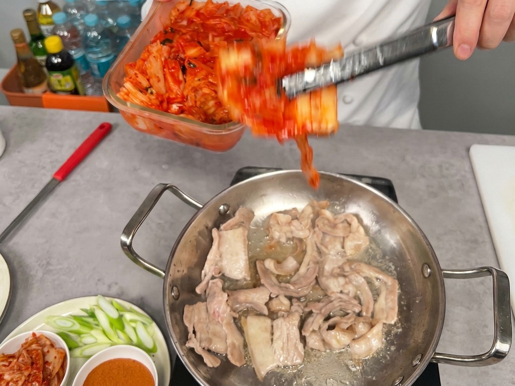 豚肉の入った鍋に、真っ赤な熟成キムチを加える様子。