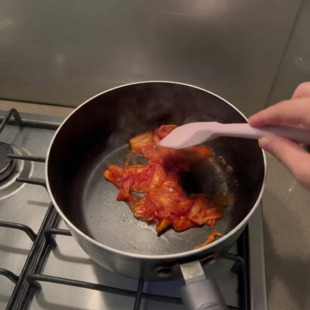 ピンクのスパチュラで鍋の中のキムチを炒めている手元の様子