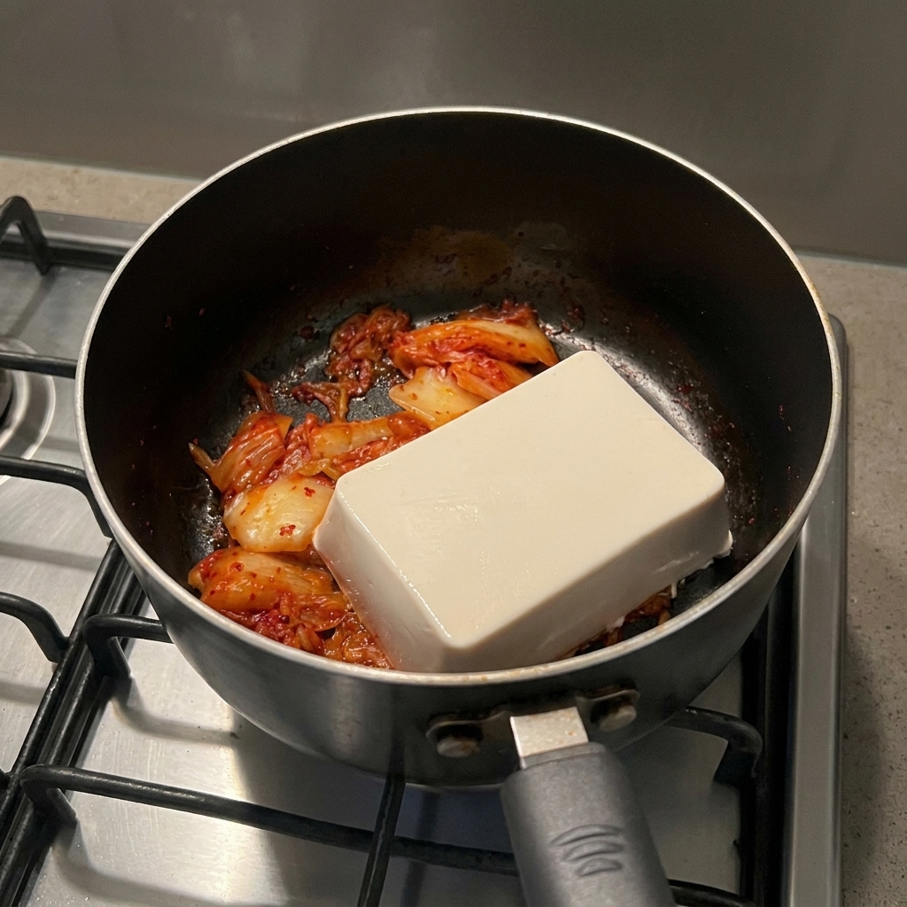 炒めたキムチの上に、丸ごと一丁の白い絹ごし豆腐が乗っている様子
