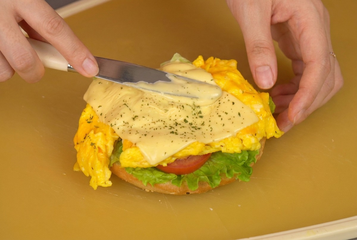 フライ返しでチーズスクランブルエッグを野菜をのせたバンズに移している様子
