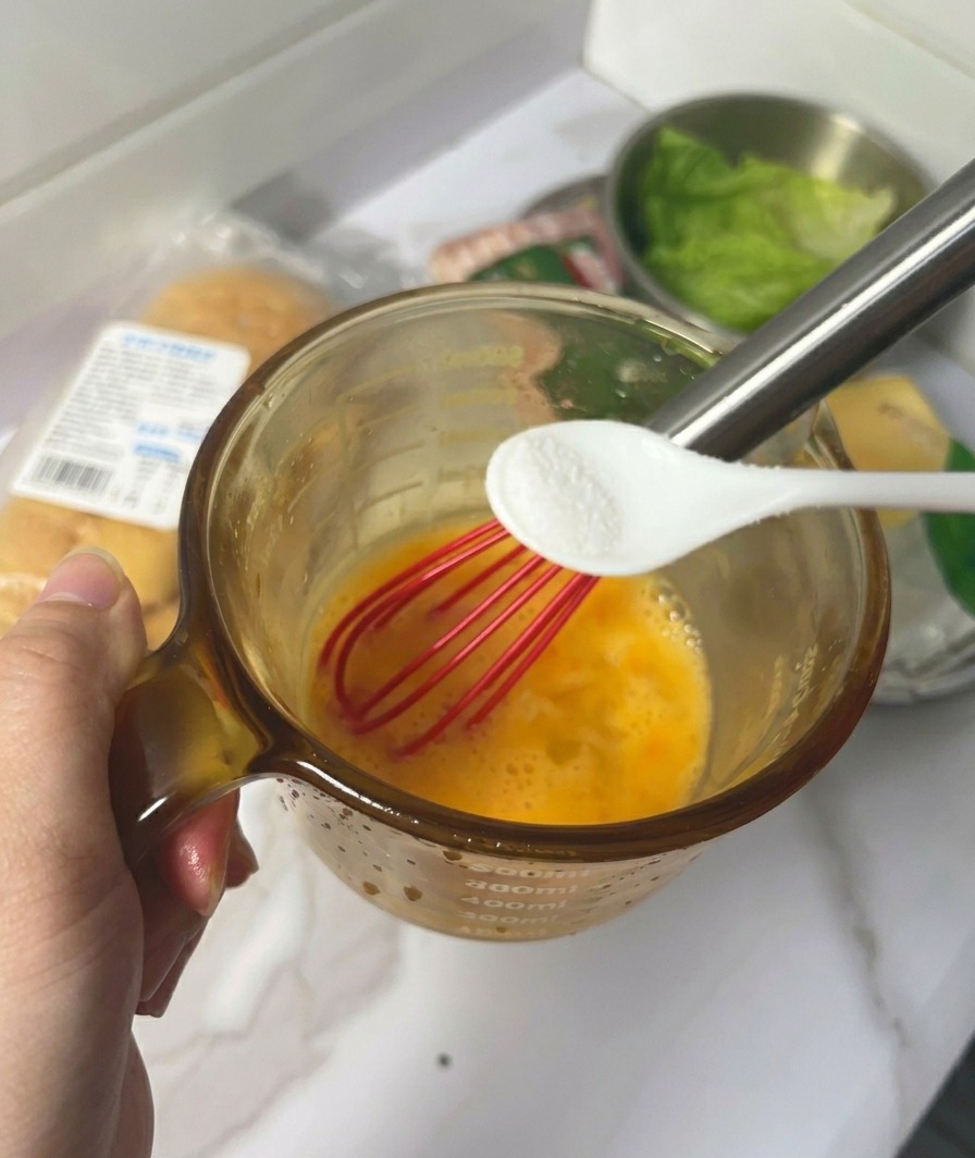 溶き卵が入ったカップの上で、小さなスプーンで塩を加えている手元。