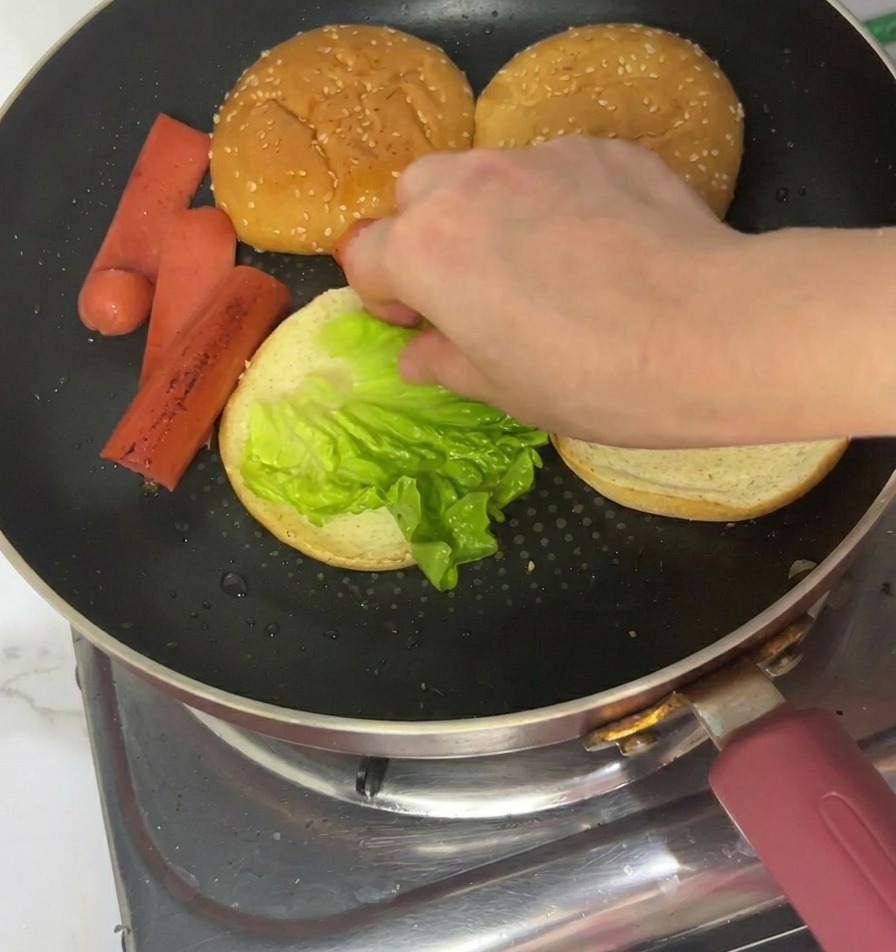 トーストしたバンズの上に、鮮やかな緑色のレタスをのせている手元。
