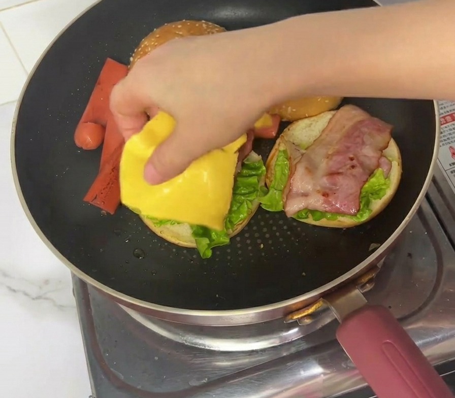 温かいベーコンの上に、四角いスライスチーズをのせている様子。