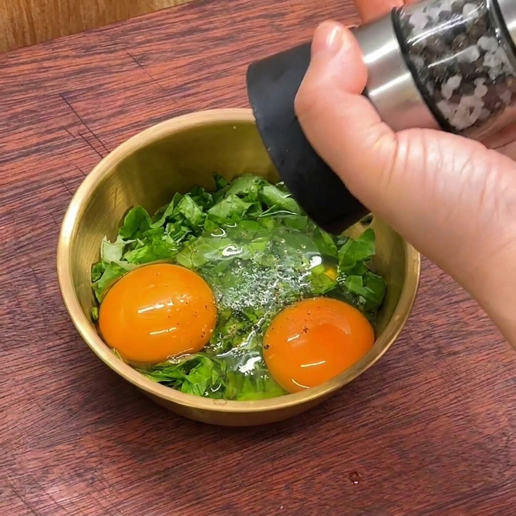ボウルに入れた2つの生卵とレタスの細切りにペッパーミルで黒胡椒を振っている様子。