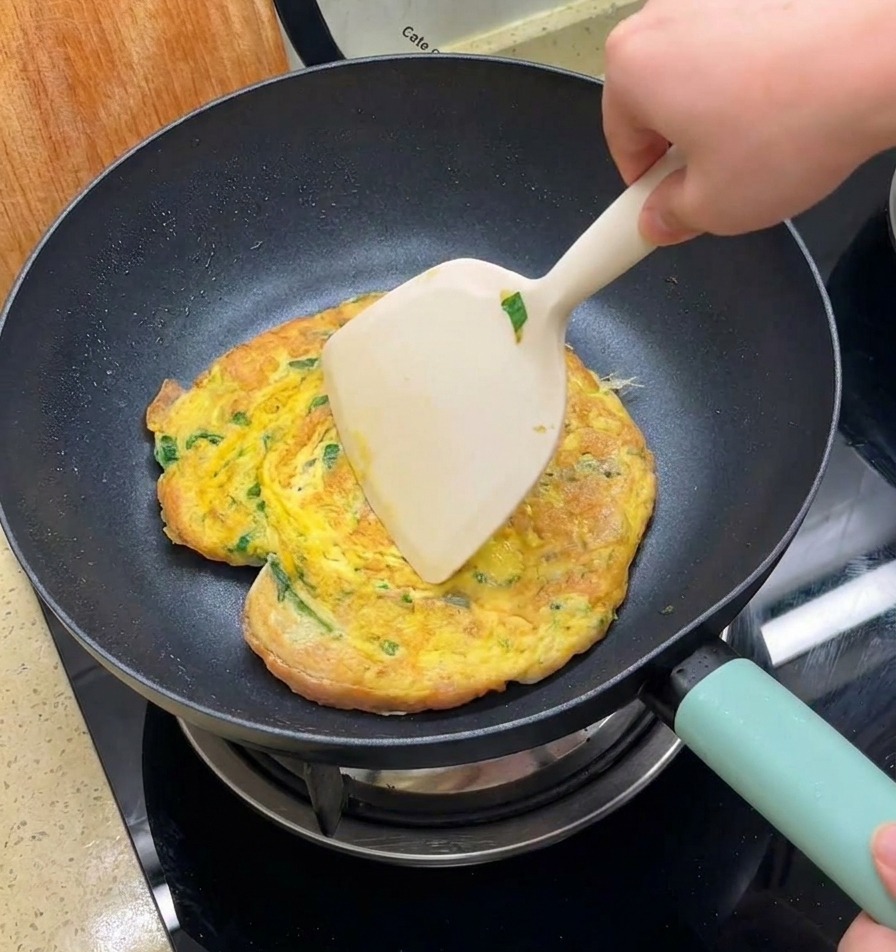 大きめのフライ返しを使い、フライパンの中で卵とバンズをひっくり返している様子。