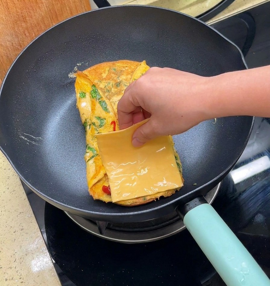 ソースをかけた卵の上に、四角いスライスチーズをのせている様子。