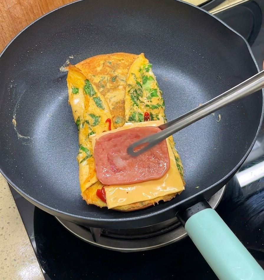 トングを使って、チーズの上にカリカリのベーコンをのせている様子。