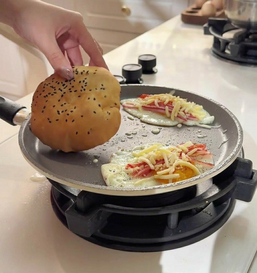 フライパンで焼いている卵とチーズの上に、ふわふわのバンズを乗せている様子
