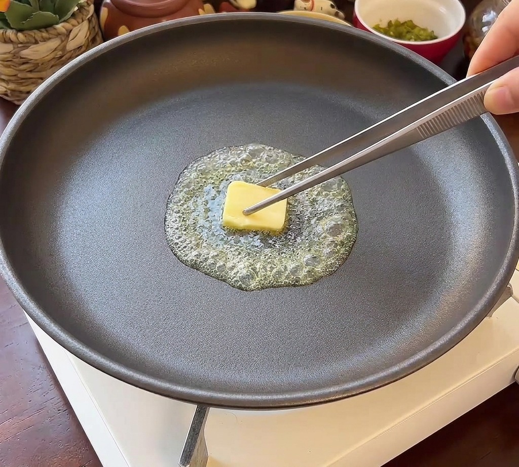 溶けたバターが広がるフライパンに、半分に切ったバーガーバンズ2つを断面を下にして置いている様子。