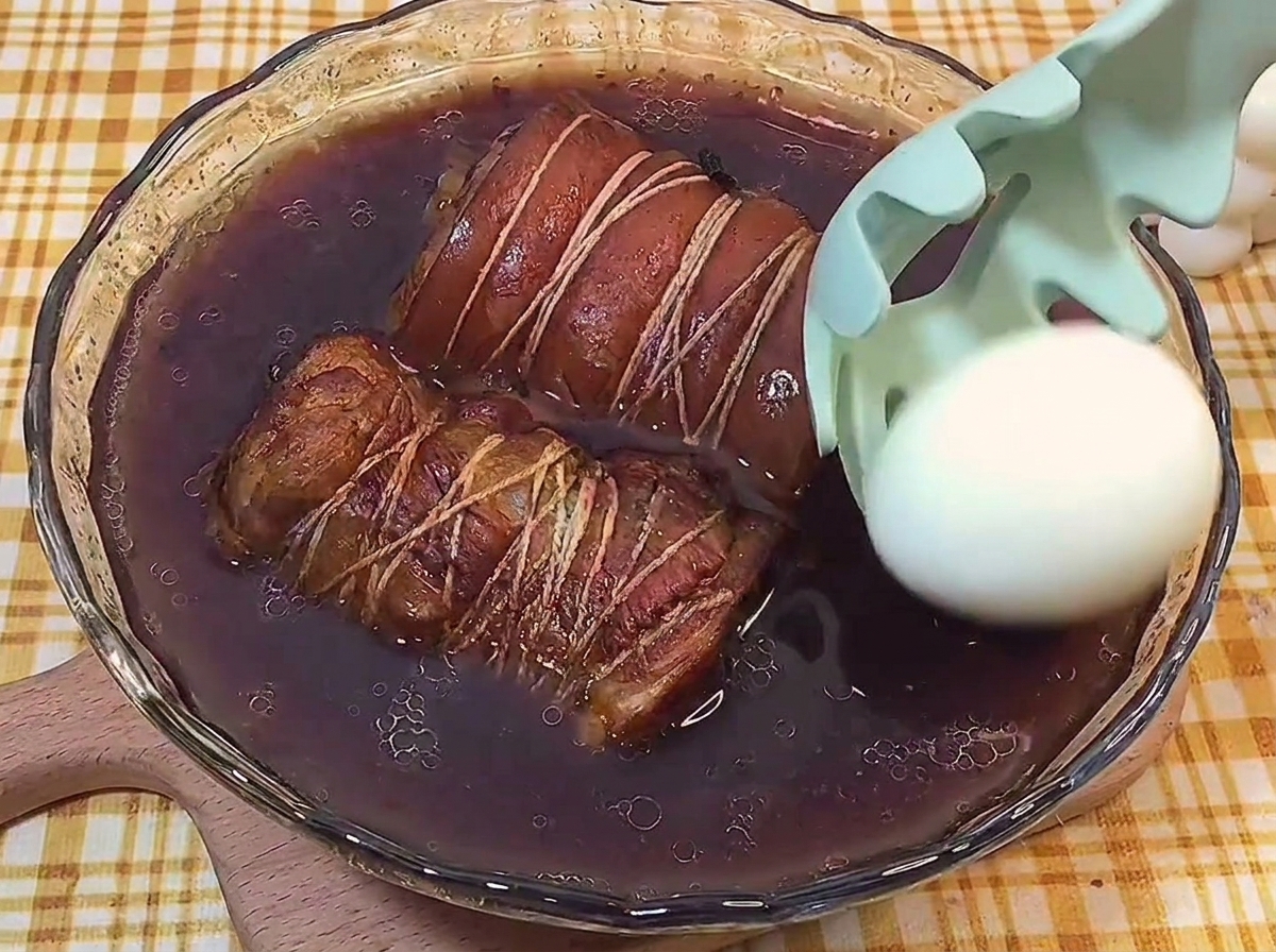 耐熱容器に入った煮汁とチャーシューの中に、殻を剥いたゆで卵をそっと入れている様子。