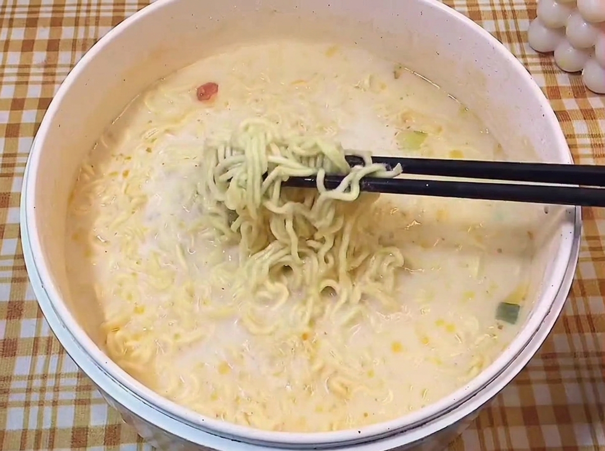 黒い箸で、白濁したスープの中からウェーブのかかった麺を持ち上げている様子。