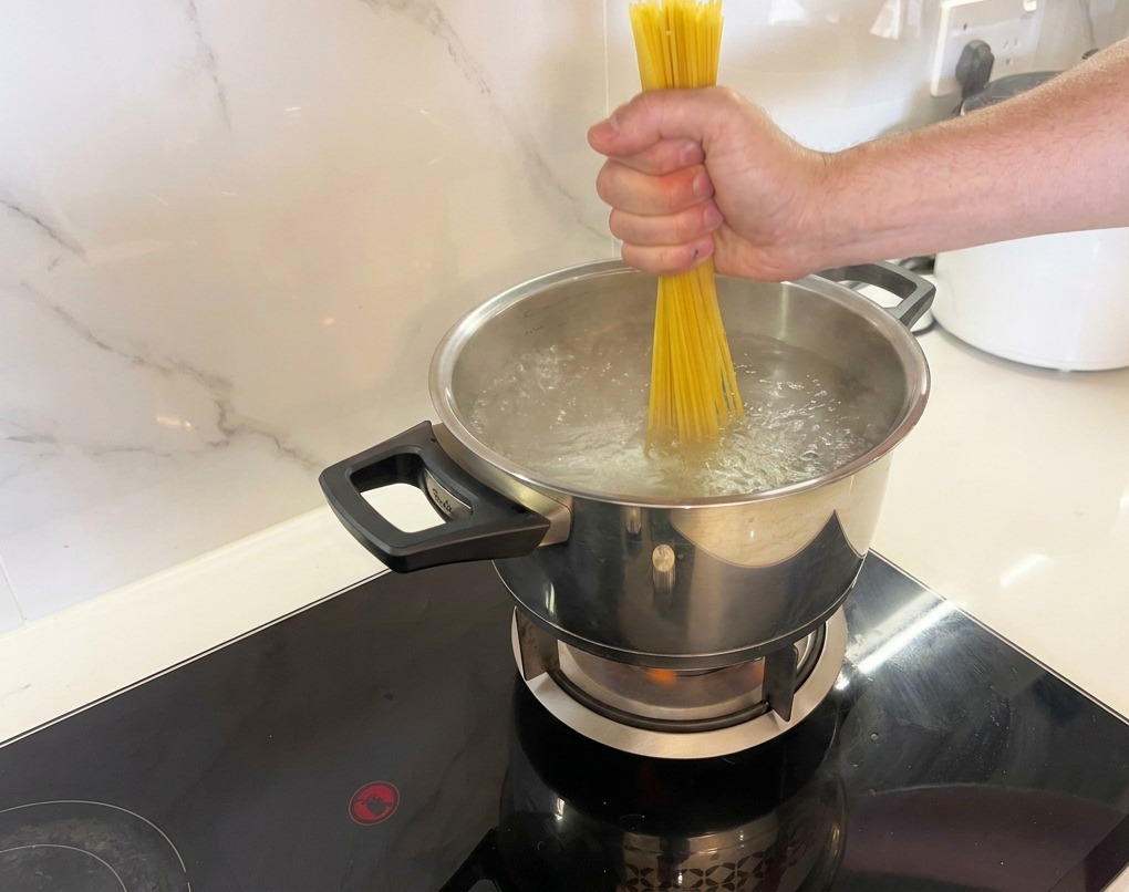 沸騰したお湯の中に、乾燥スパゲッティを束ねて入れ、押し込む様子。