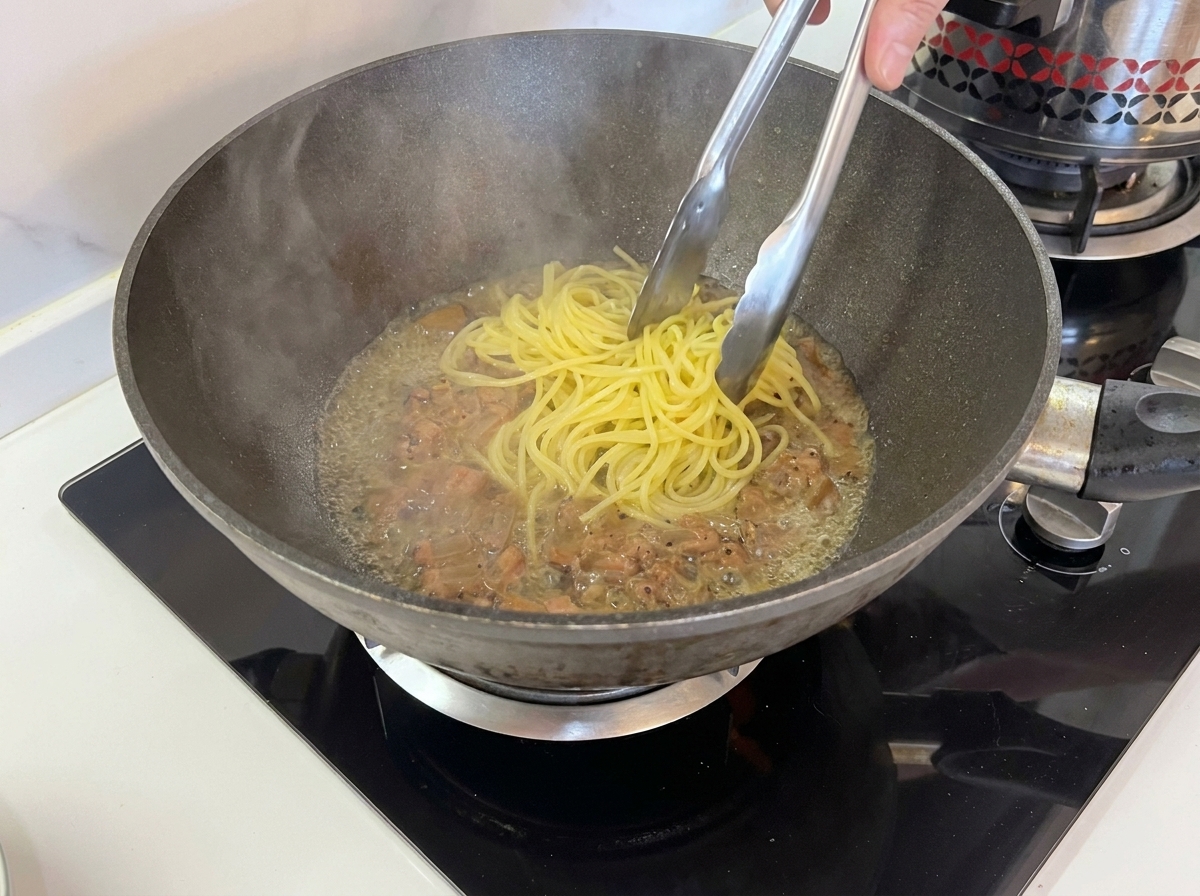 トングを使い、茹で上がったスパゲッティを鍋からグアンチャーレの入ったフライパンへ直接移す様子。