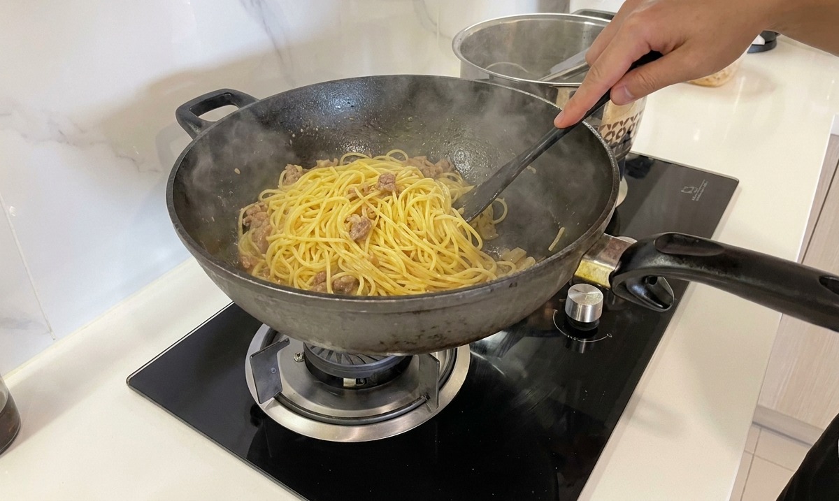 手早くパスタを混ぜ合わせ、クリーミーに乳化したカルボナーラソースを仕上げる様子。