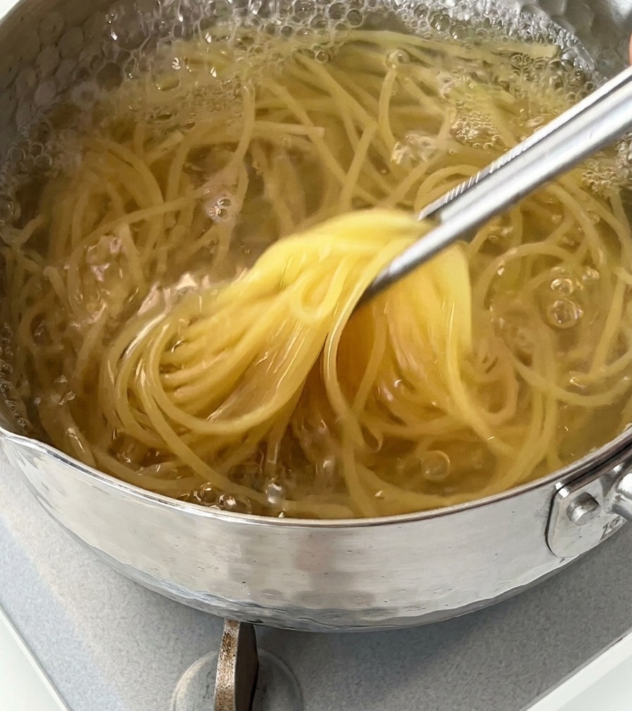 沸騰した鍋からトングでスパゲッティを持ち上げている様子。