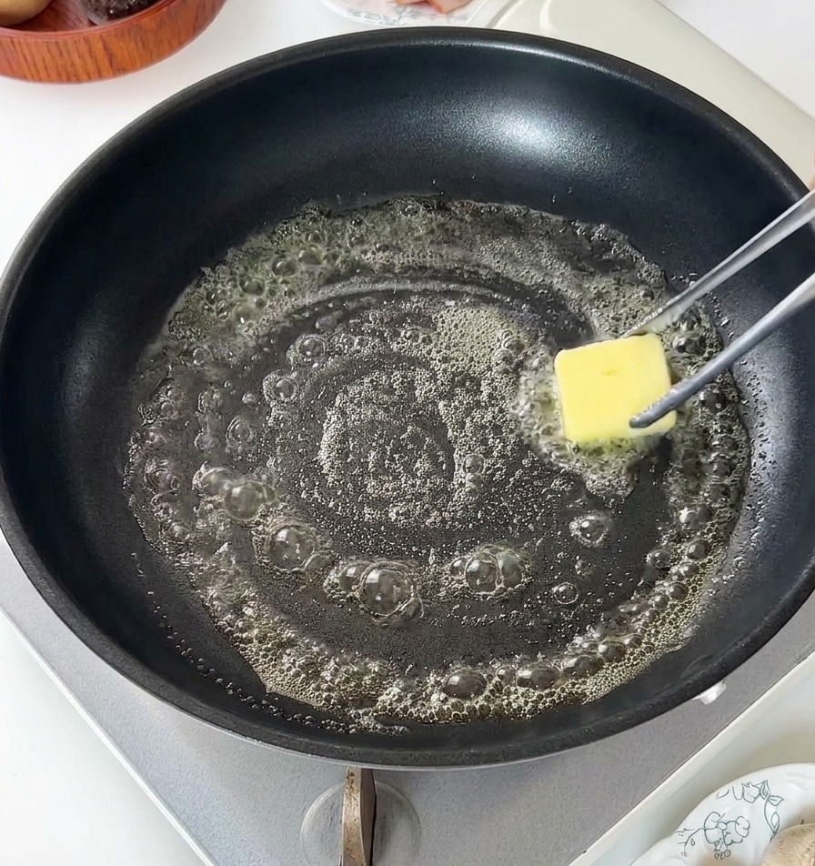 黒いフライパンの中でバターが溶けて泡立っている様子。