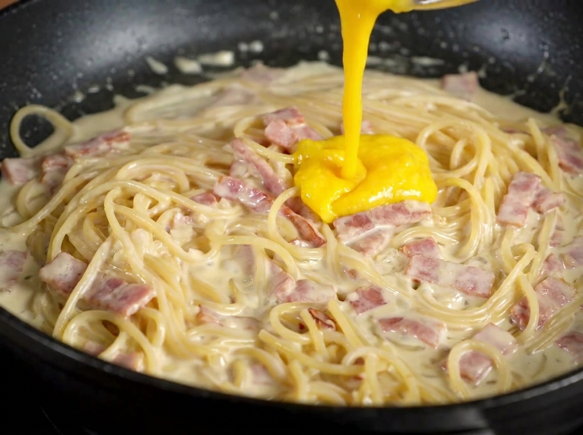 火を止めたパスタの上から卵黄とチーズのミックスをかけている様子