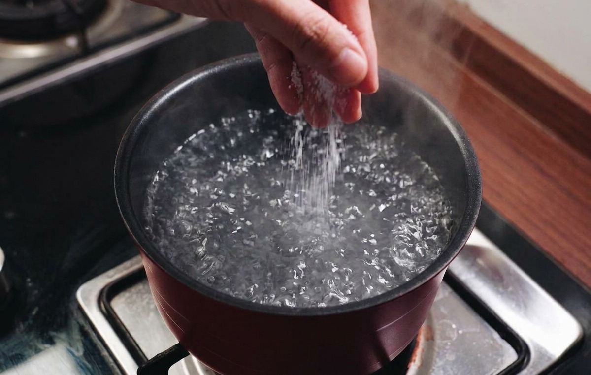 コンロの上の鍋で勢いよく沸騰しているお湯に塩を振りかけている様子。