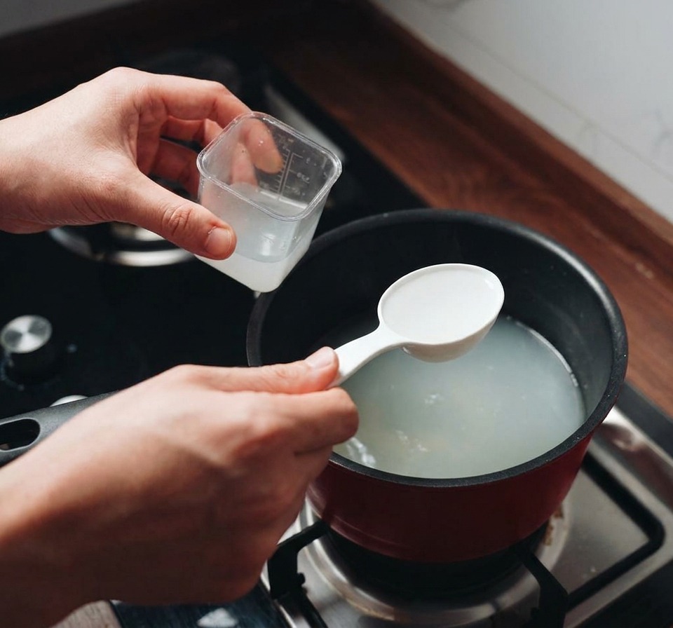 コンロの上の鍋から、白濁したパスタの茹で汁をお玉ですくい取っている様子。