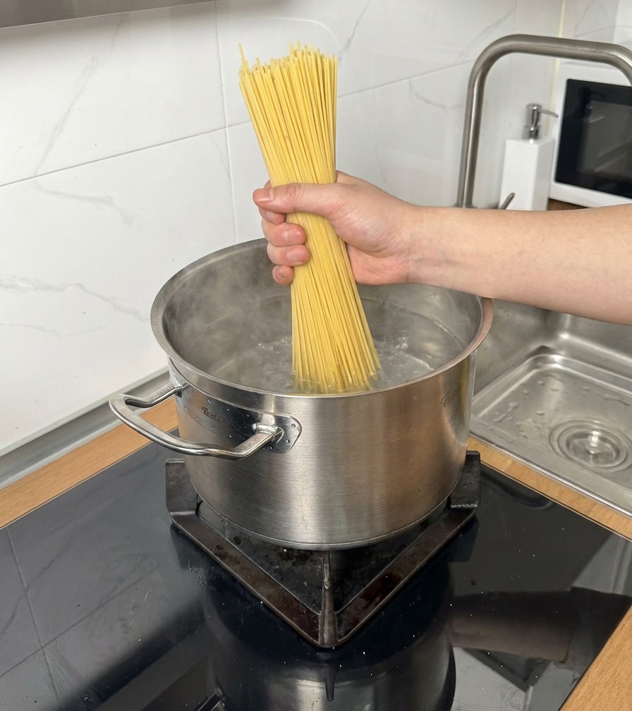 沸騰した鍋の湯に、乾燥スパゲッティの束を入れる様子。