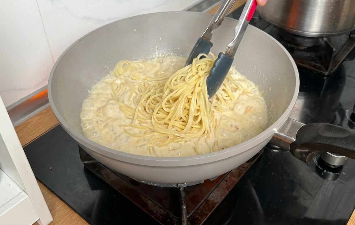 茹で上がったロングパスタをトングで直接フライパンのソースの中へ移す様子。