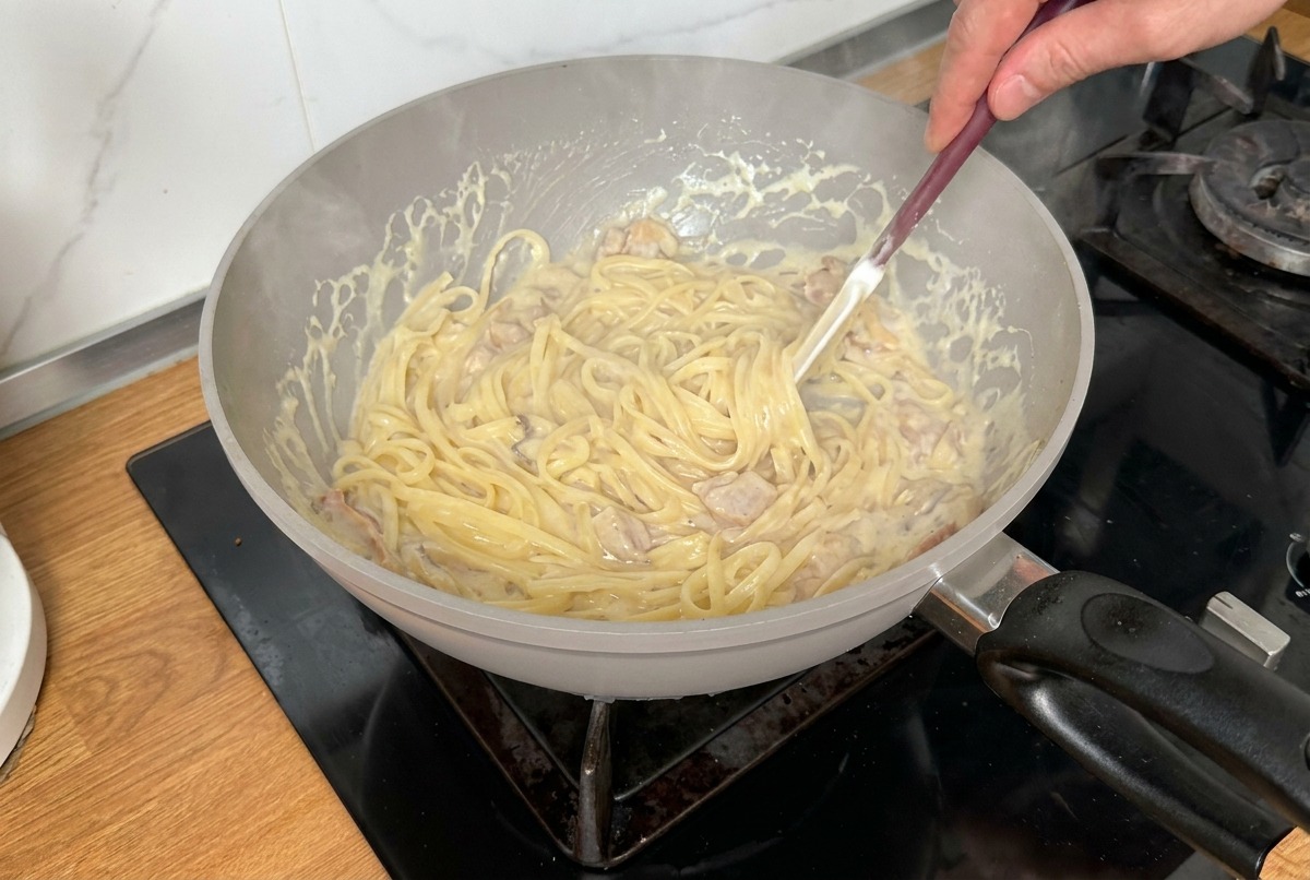 パスタ全体にクリームソースが行き渡るよう、フライパンの中でトングを使って混ぜ合わせている様子。