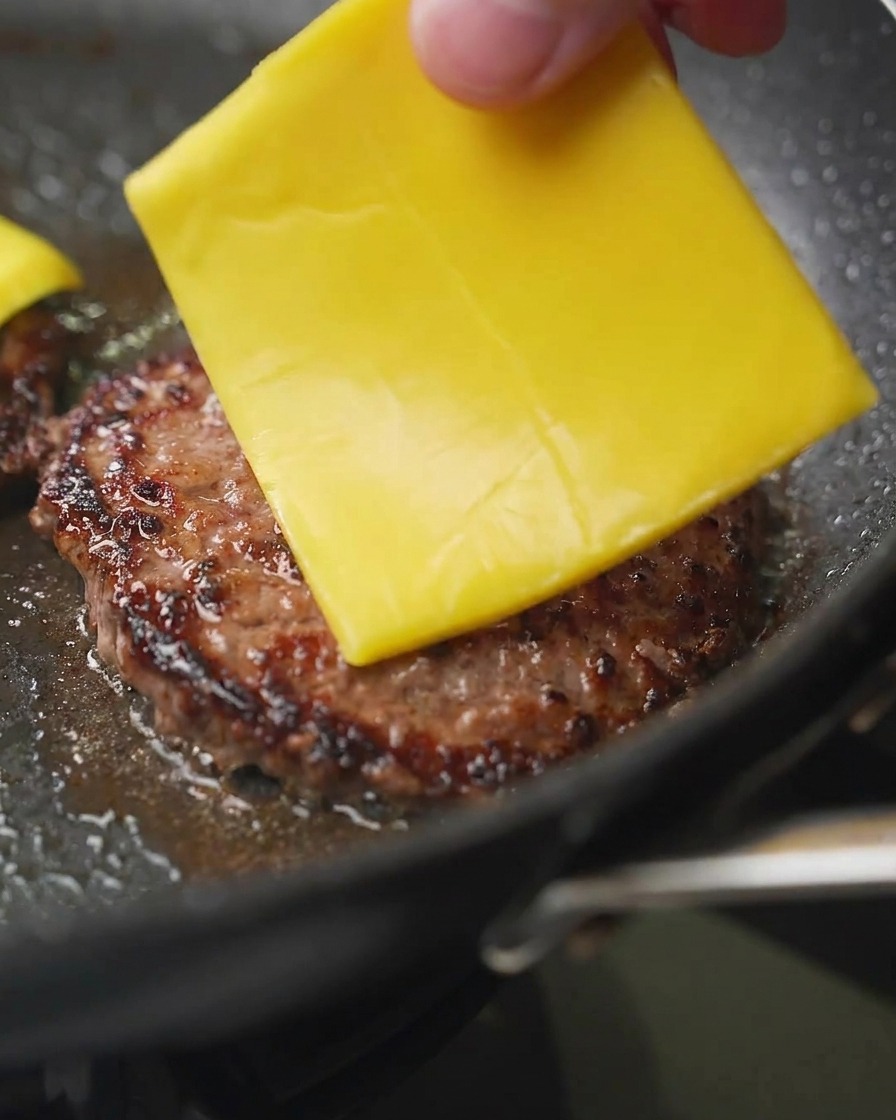 フライパンの中で焼き色のついたパティの上に、チェダーチーズを1枚ずつのせている様子。