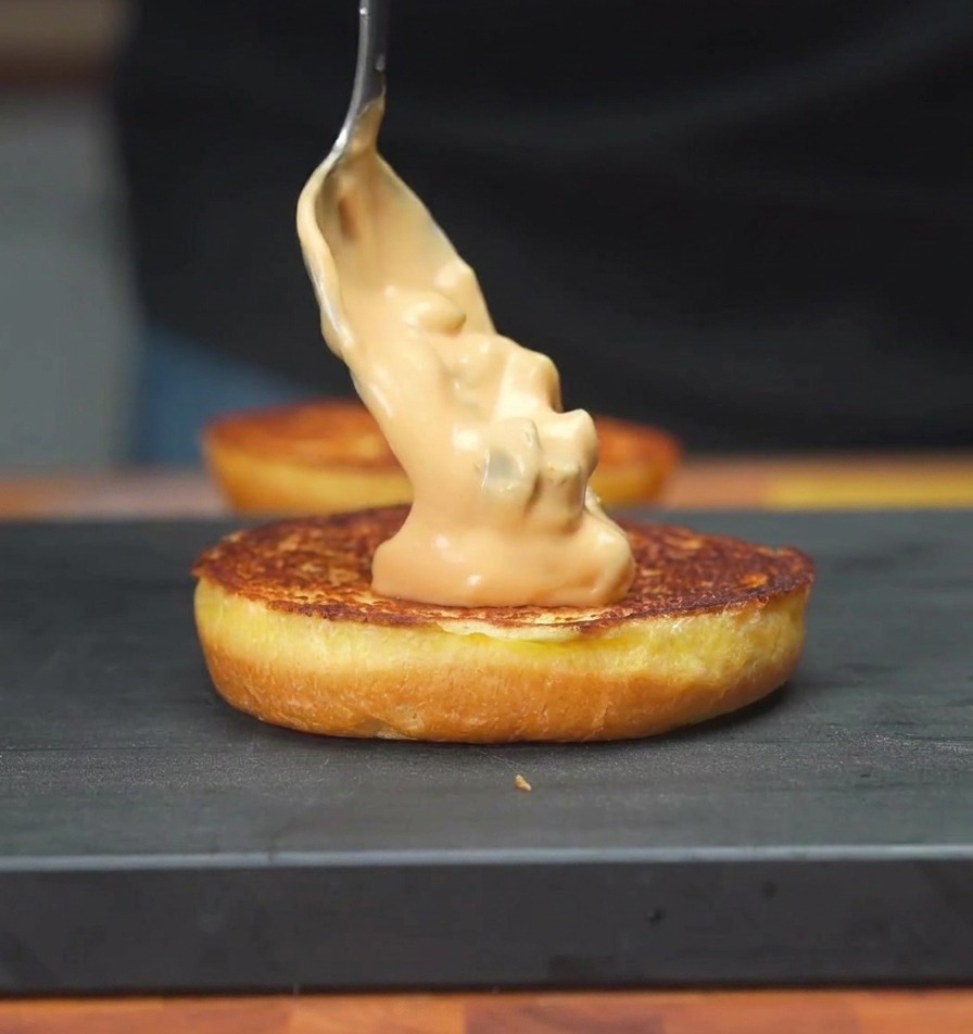 焼いたバンズに、スプーンでオレンジ色の特製ソースを塗っている様子。