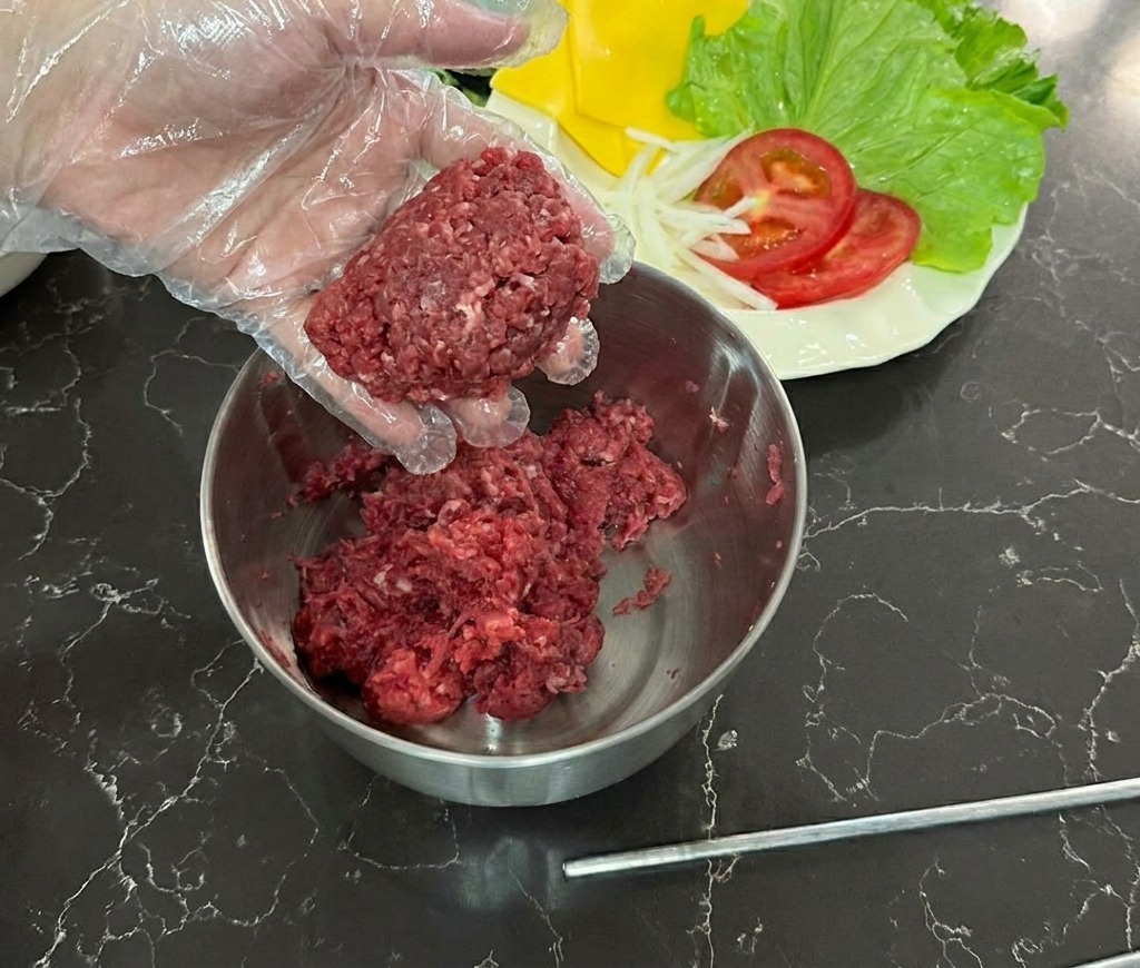 ビニール手袋をした手で、ボウルの上で牛挽肉を丸めている様子