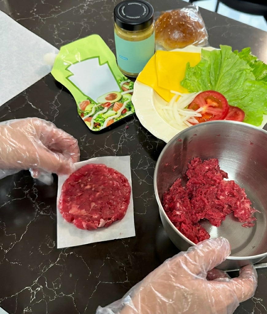 クッキングシートの上で牛挽肉のボールを平たく押し潰し、円形のパティにしている様子