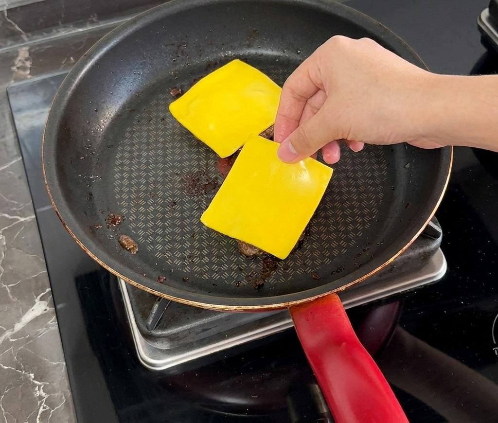 焼き上がったパティの上に、四角いスライスチーズをのせている様子