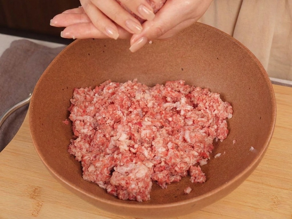 ボウルの上で、牛挽肉を丸いボール状に整えている手の様子。