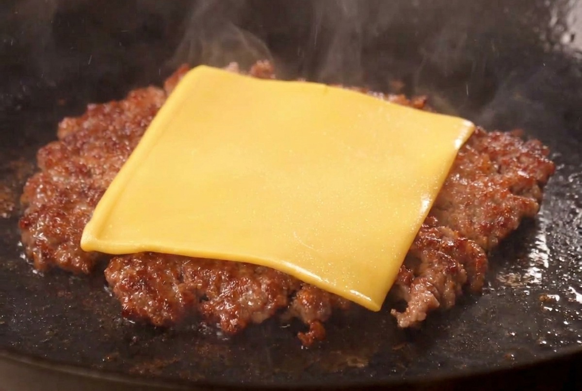 フライパンの中で、こんがり焼けたパティの上にアメリカンチーズがとろけている様子。