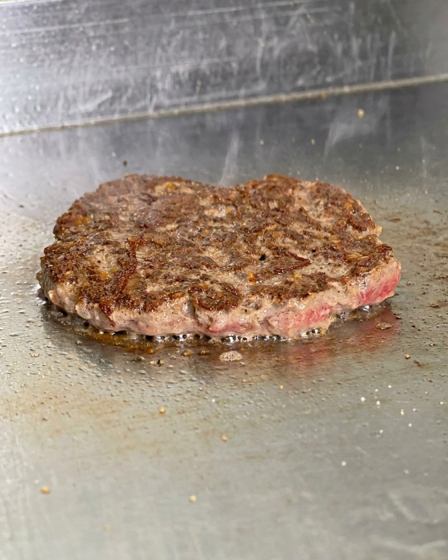 鉄板の上で裏返されたパティ。表面に濃い茶色の香ばしい焼き色がつき、脂が泡立っている様子。