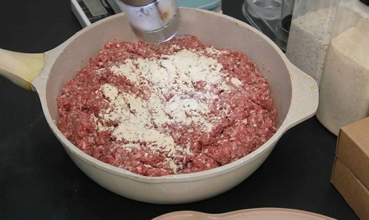 黒い手袋をした人が、電動ミルで海塩を挽肉に加えている様子。