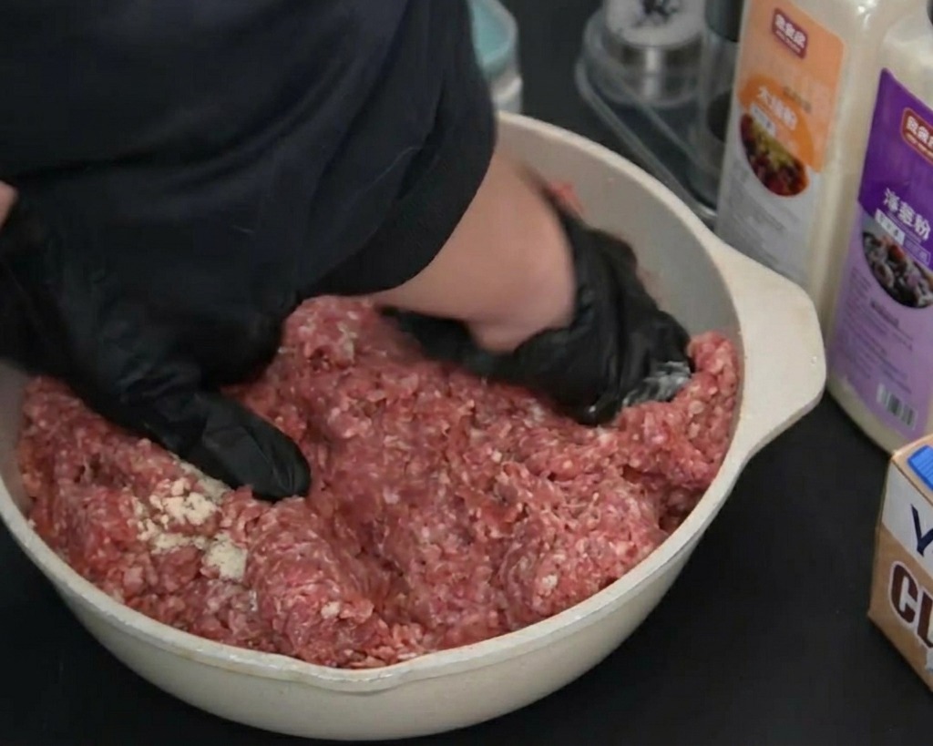 手袋をした手で、肉とスパイスをしっかりと混ぜ合わせ、こねている様子。