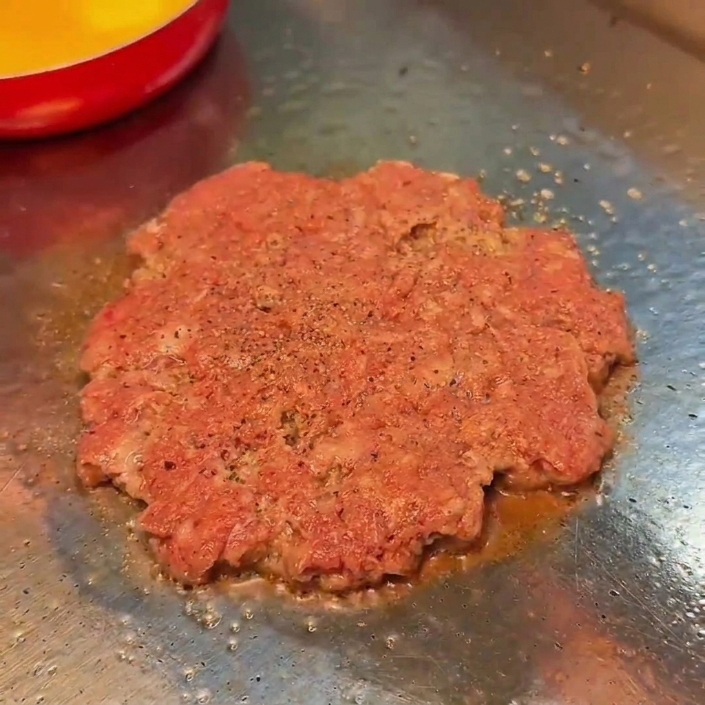 グリルで焼いているパティに塩こしょうを振る様子。