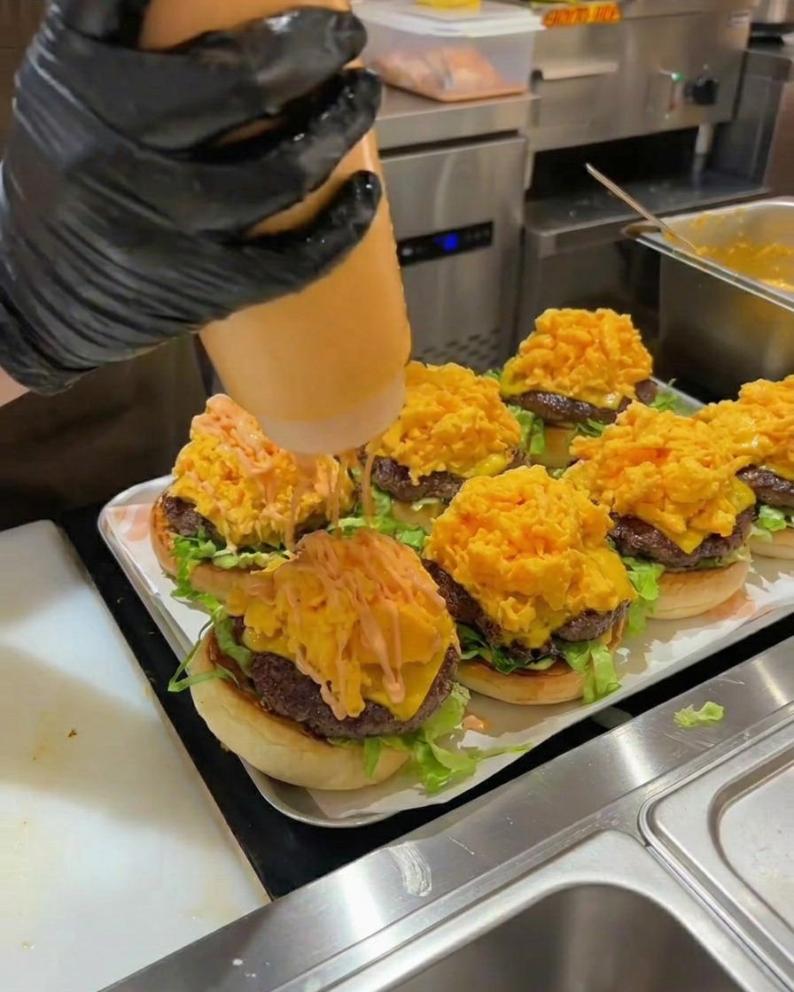 組み立てたバーガーの卵の上にソースをかけて仕上げる様子。