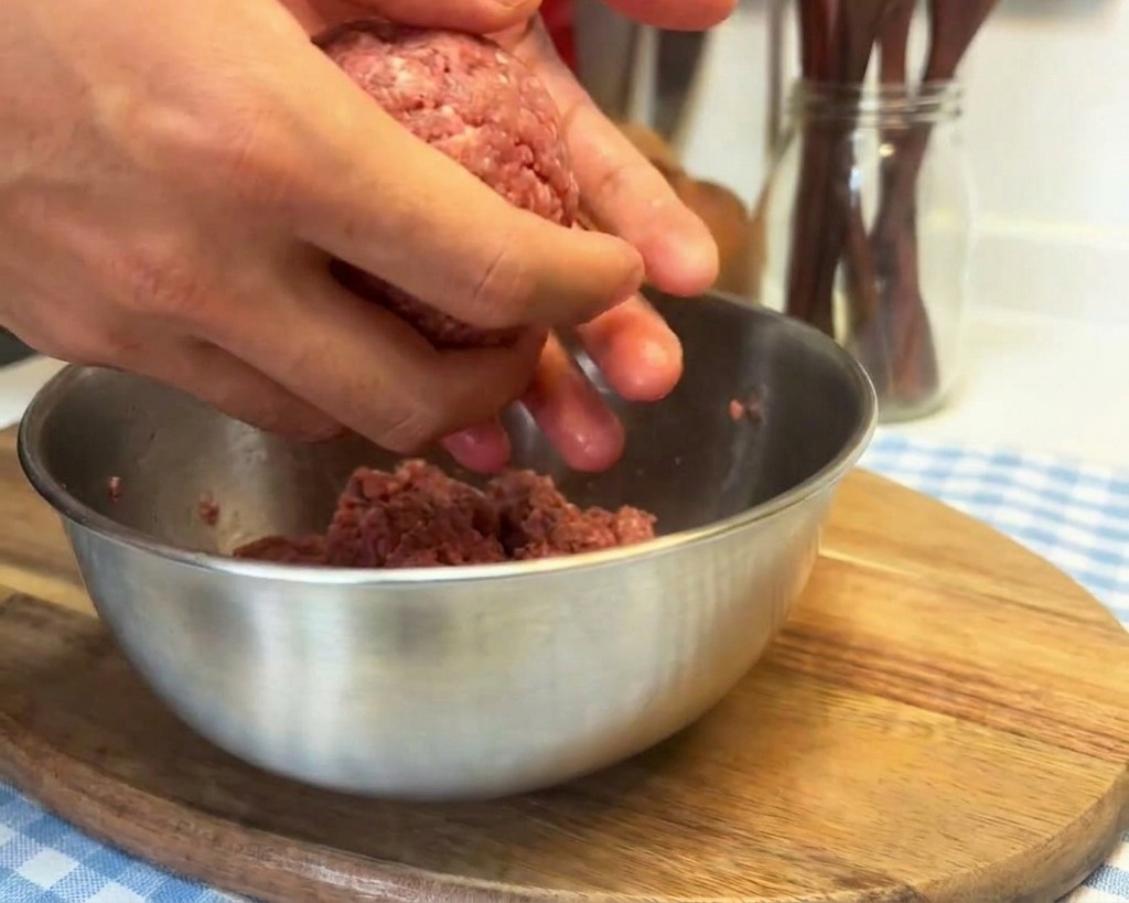 ひき肉の塊を手のひらに打ち付けて、成形前に肉の質感を整えている様子。
