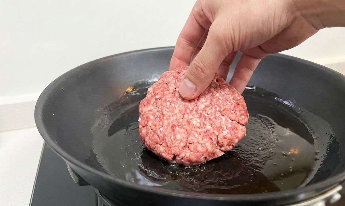 熱したフライパンに油を引き、丸いパティを並べて焼き始めている様子。