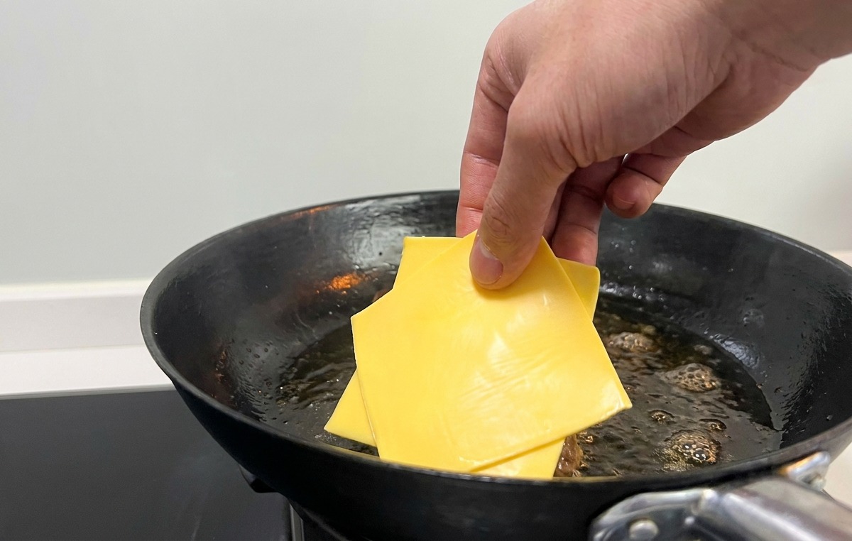 フライパンの中のパティの上に、四角いスライスチーズを乗せている様子。