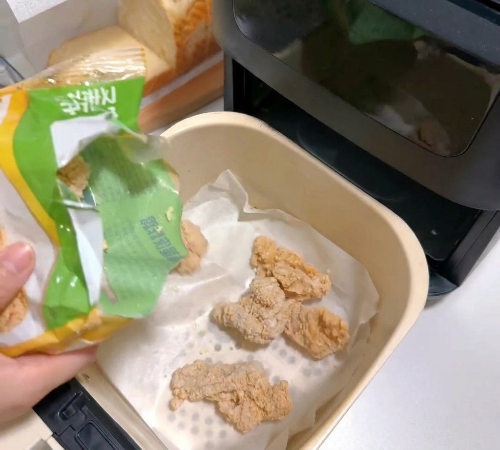 クッキングシートを敷いたノンフライヤーのバスケットに冷凍チキンを入れる様子。