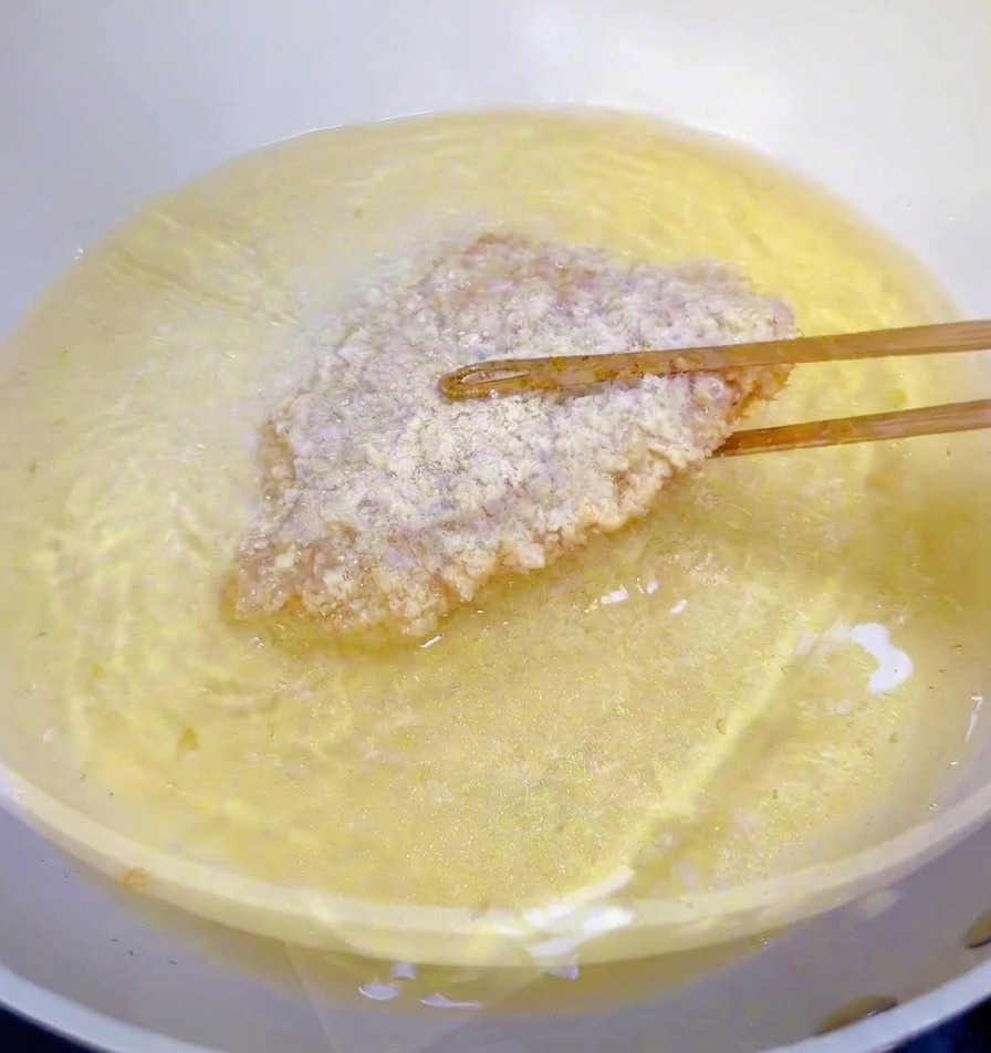 熱い油が入った鍋に、菜箸を使ってパン粉の付いたチキンフィレを入れている様子。
