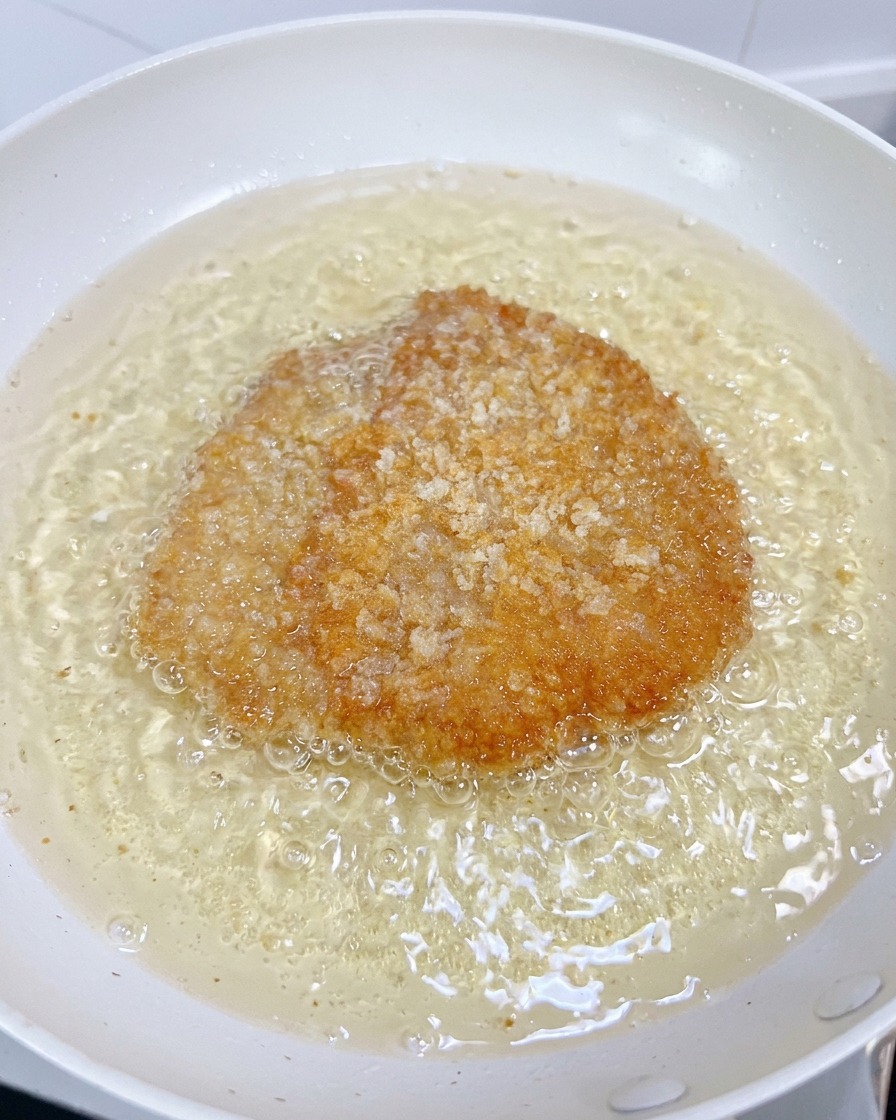 白い鍋の泡立つ油の中で、衣がこんがりと揚がったチキンフィレ。