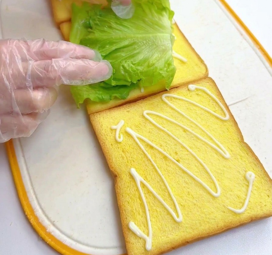 ドレッシングをかけた食パンの上に、鮮やかな緑色のレタスをのせている手。