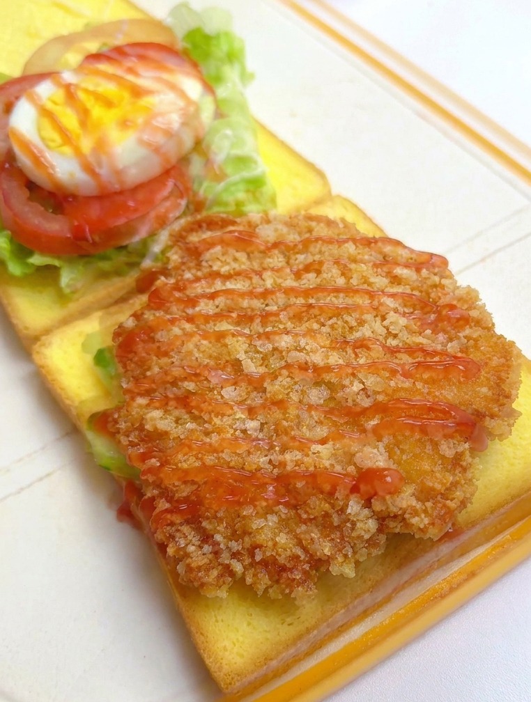 パンの上のチキンフィレに赤いケチャップをかけている様子。