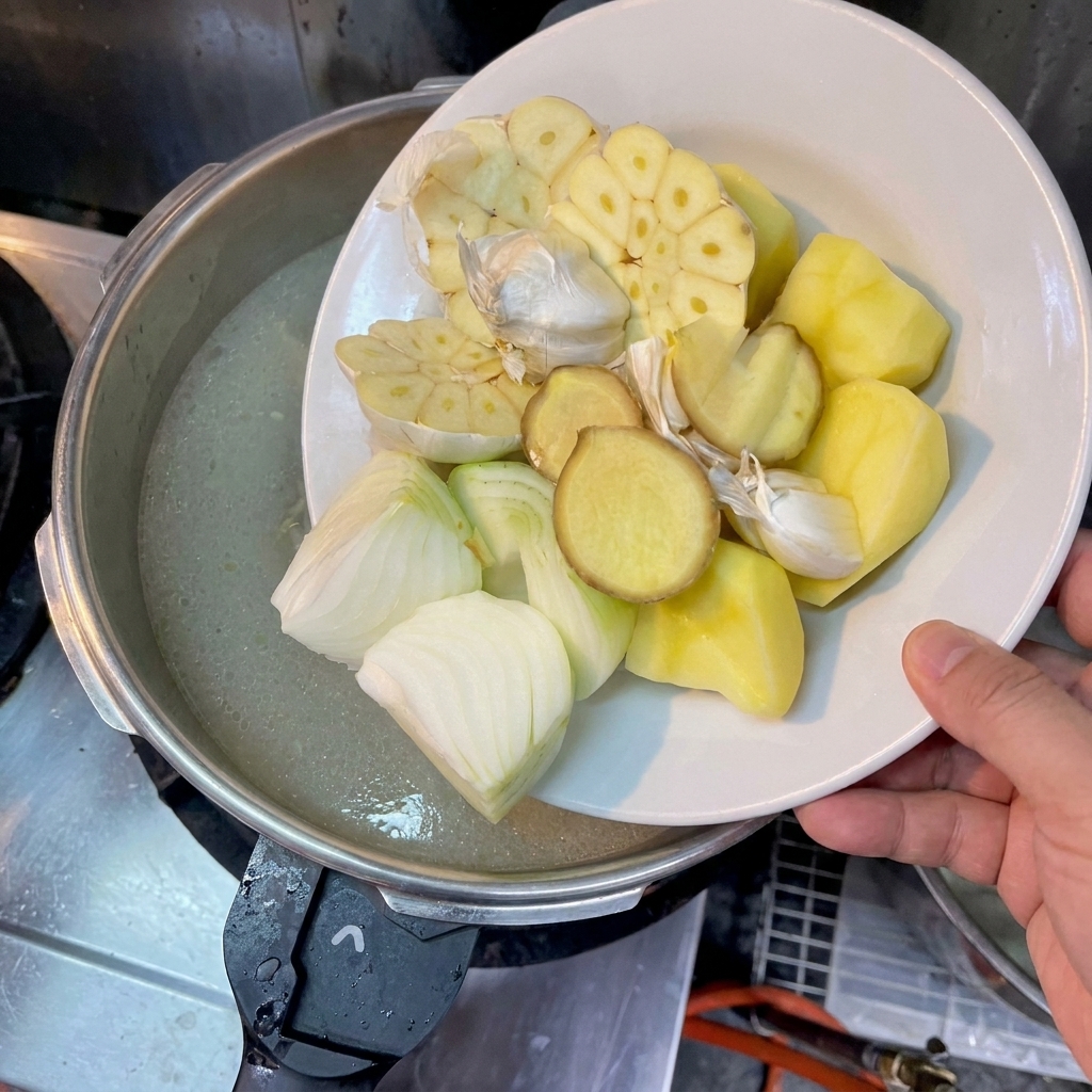 カットしたじゃがいも、玉ねぎ、生姜、にんにくを鍋に加えている手元。
