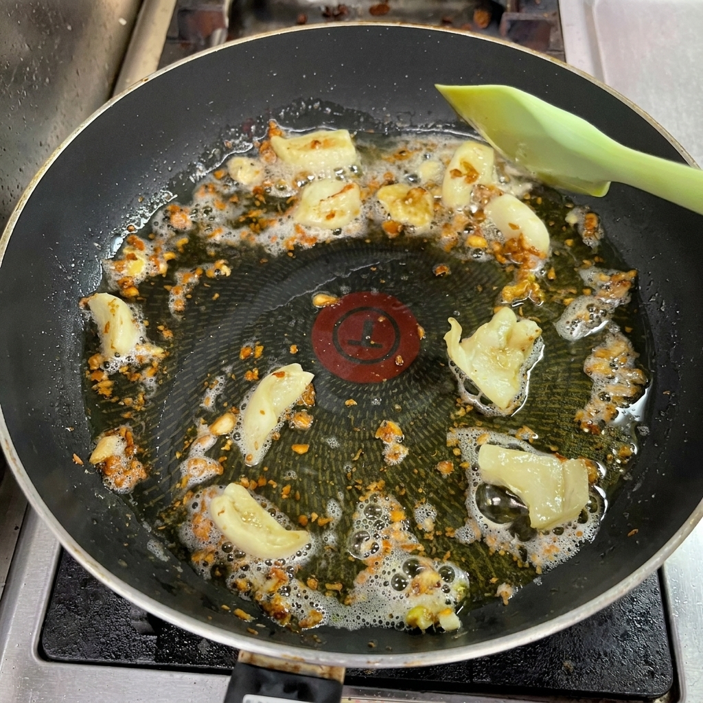 油の中のにんにくが濃い茶色に色付き、ヘラで混ぜている様子。