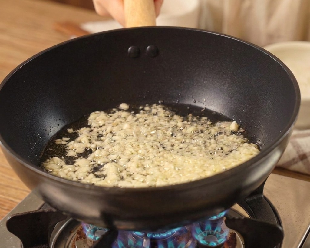 フライパンでみじん切りのニンニクが油で炒められている様子。