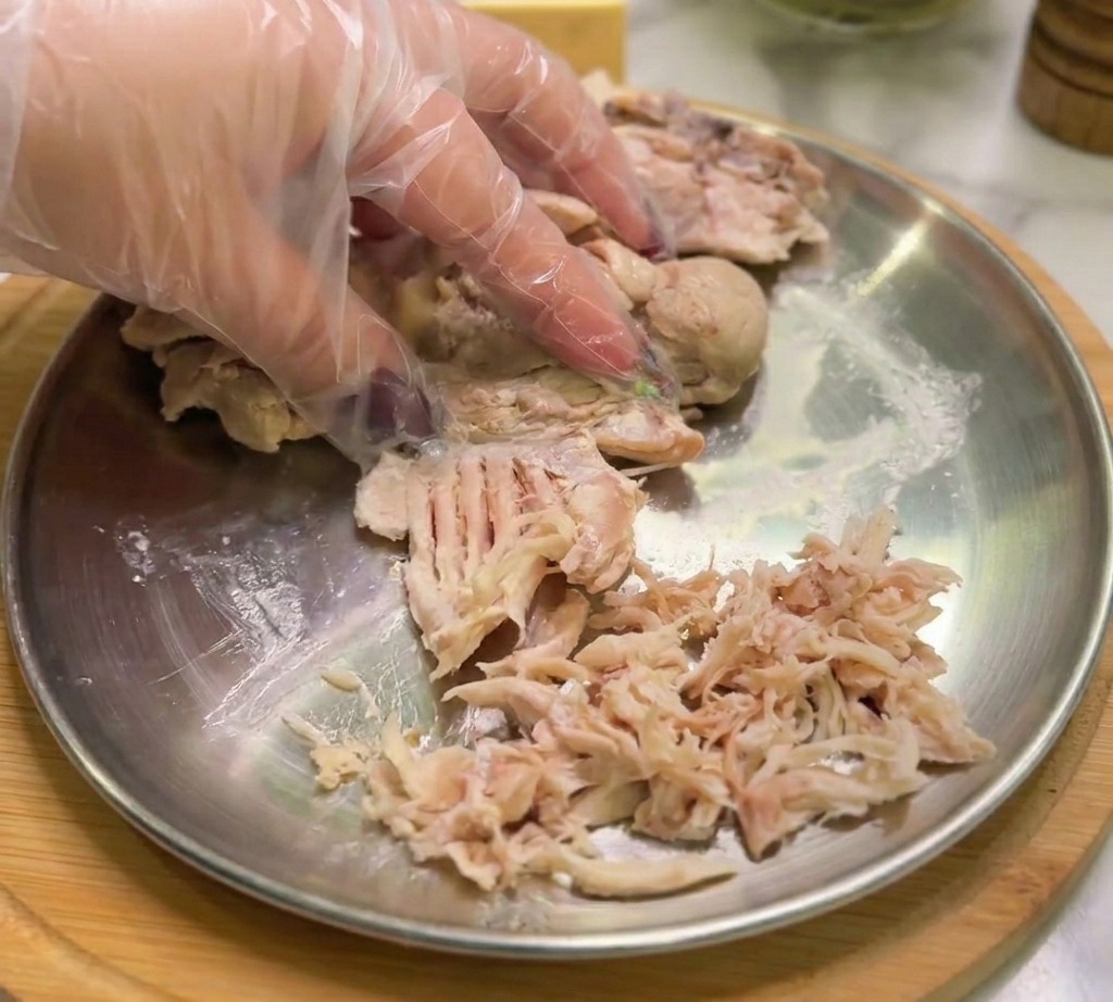手袋をはめた手で、鶏肉を繊維に沿って細かく引き裂いている様子。